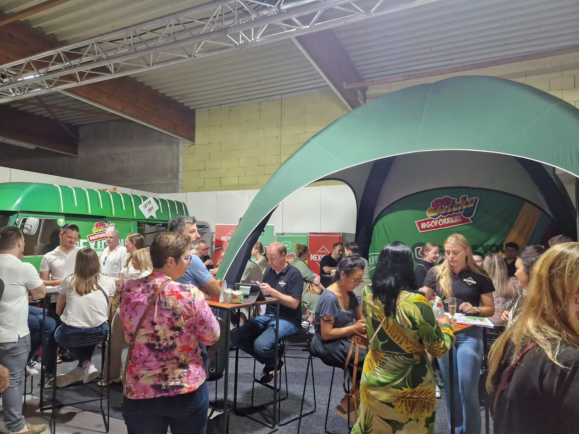 Bezoekers aan statafels onder de Attent-tent op een beurs